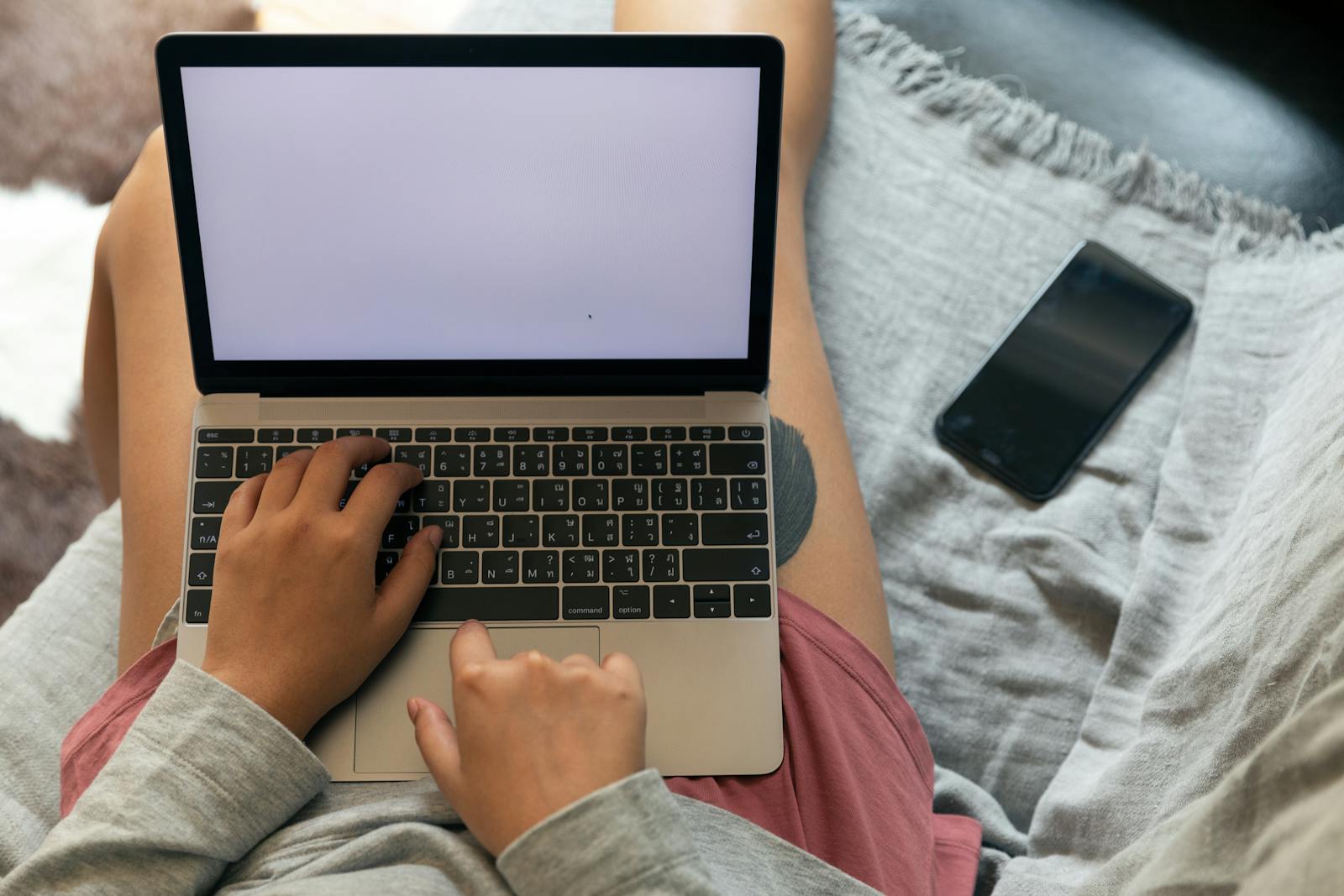 Photo by Ketut Subiyanto A person working remotely with a laptop on their lap and smartphone beside, showcasing modern work flexibility.